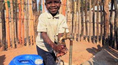 En glad pojke tvättar händerna under en vattenkran.