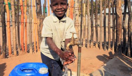En glad pojke tvättar händerna under en vattenkran.