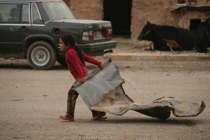 En flicka drar på en bit plåt. Fattigdom leder till brist på barnvänliga och skyddande miljöer.